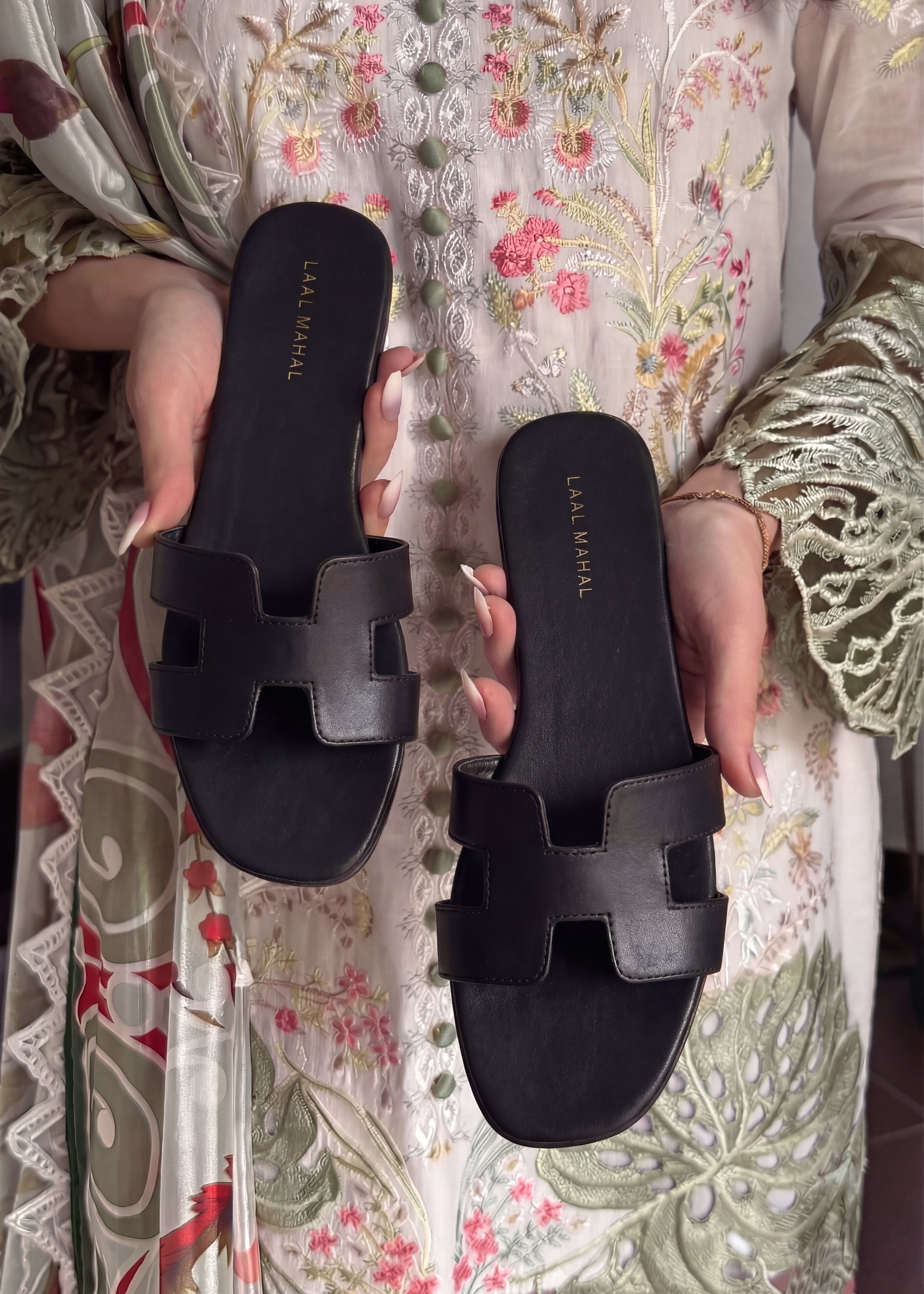 Black H style flats held up against a floral fabric background