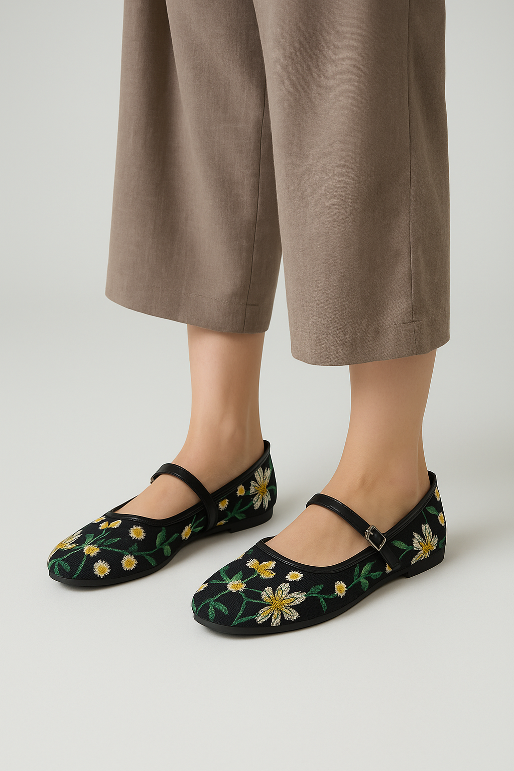 Black floral embroidered shoes worn with brown pants on a light gray background