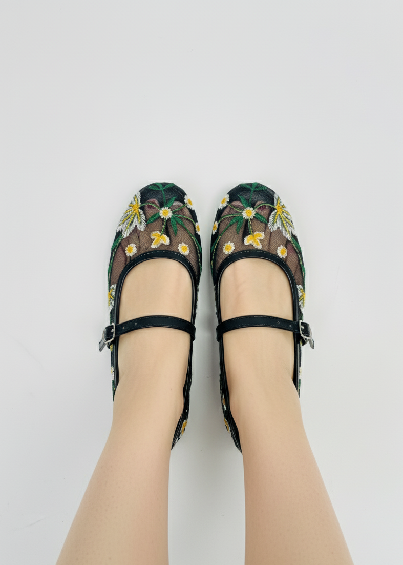 Model wearing Laal Mahal black mesh Mary Jane flats with white and yellow daisy embroidery, viewed from above on a white background