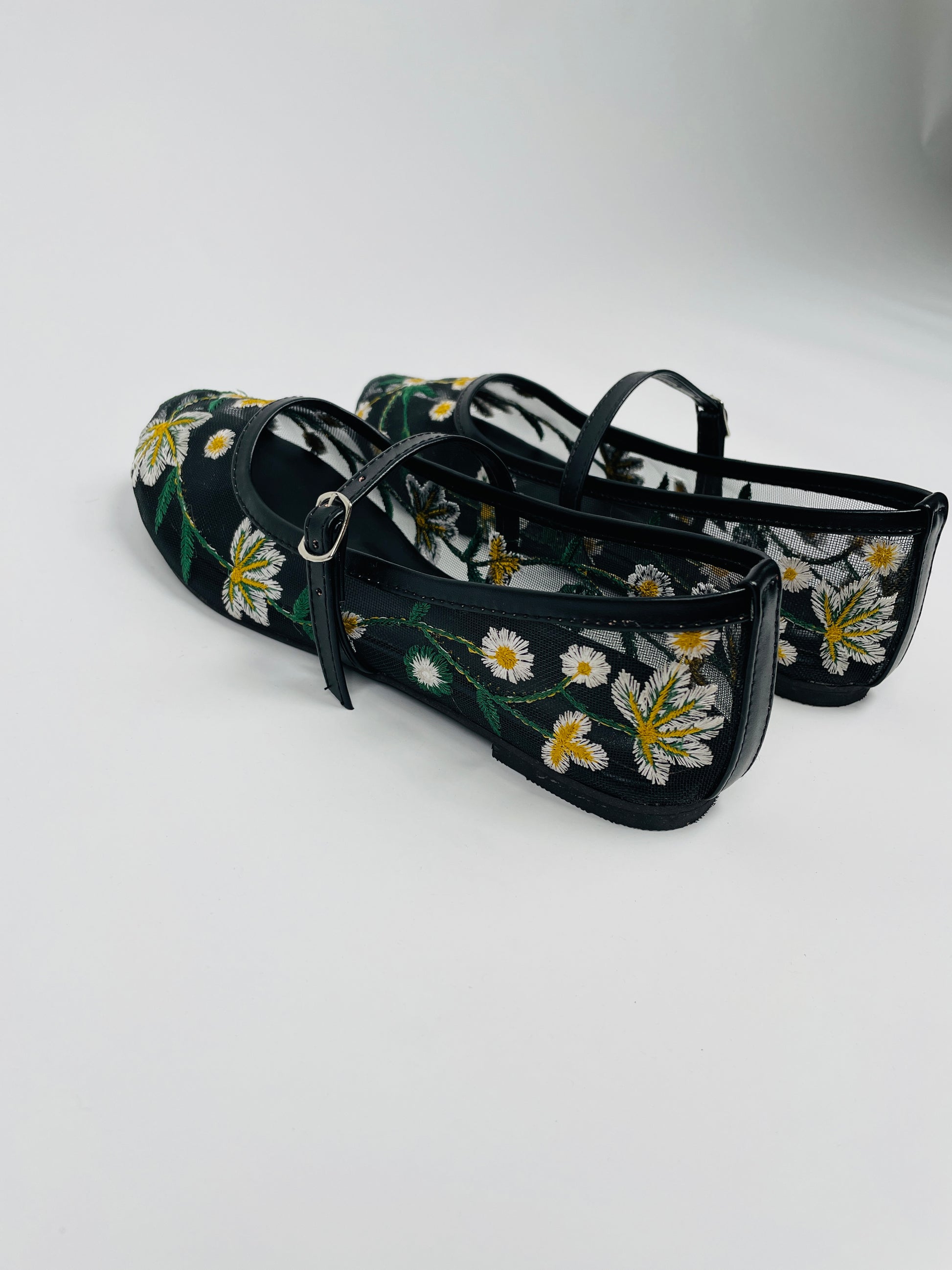 Model wearing Laal Mahal black mesh Mary Jane flats with white and yellow daisy embroidery, viewed from above on a white background