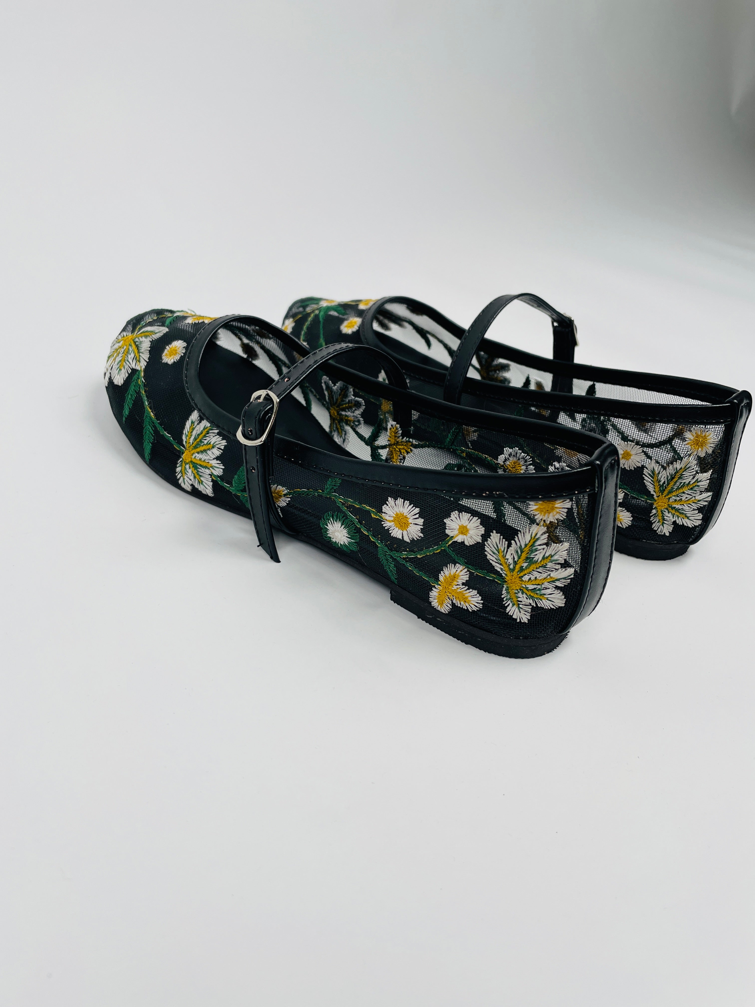 Model wearing Laal Mahal black mesh Mary Jane flats with white and yellow daisy embroidery, viewed from above on a white background