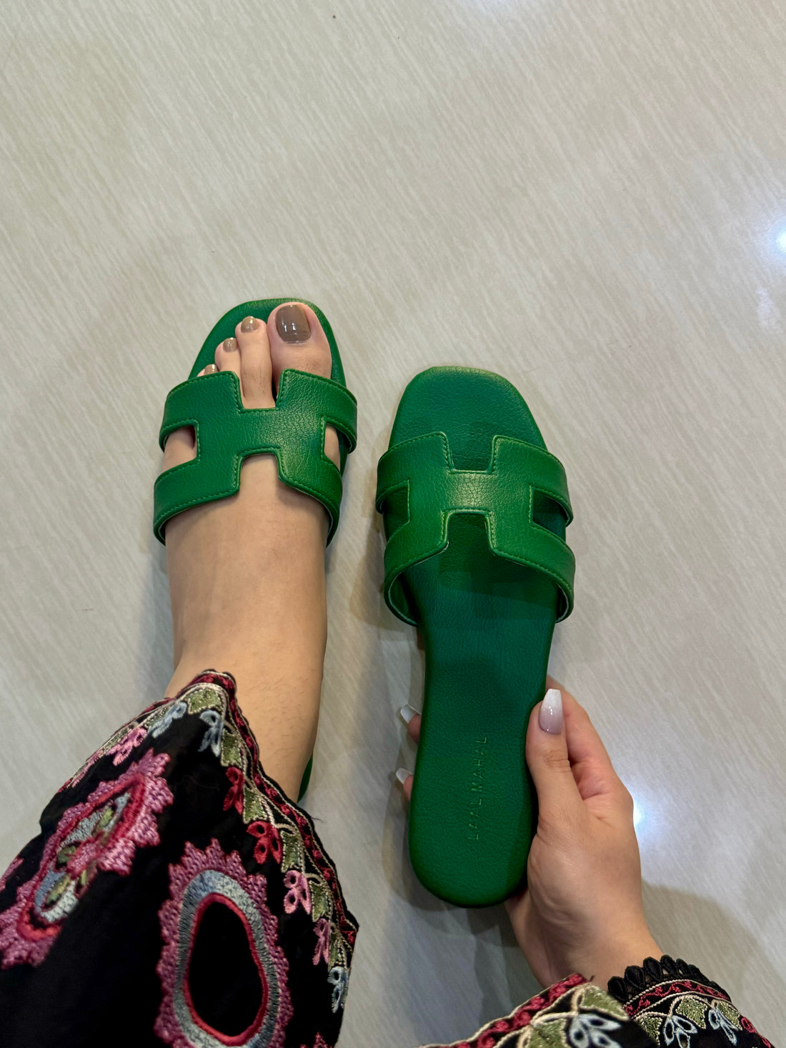 Green H style flats being worn on a light-colored floor. 