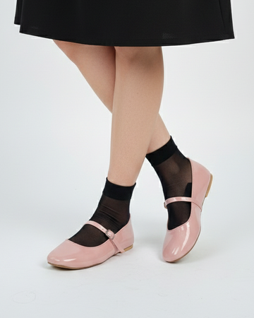 Person wearing black sheer socks with soft pink mary janes flats on a white background
