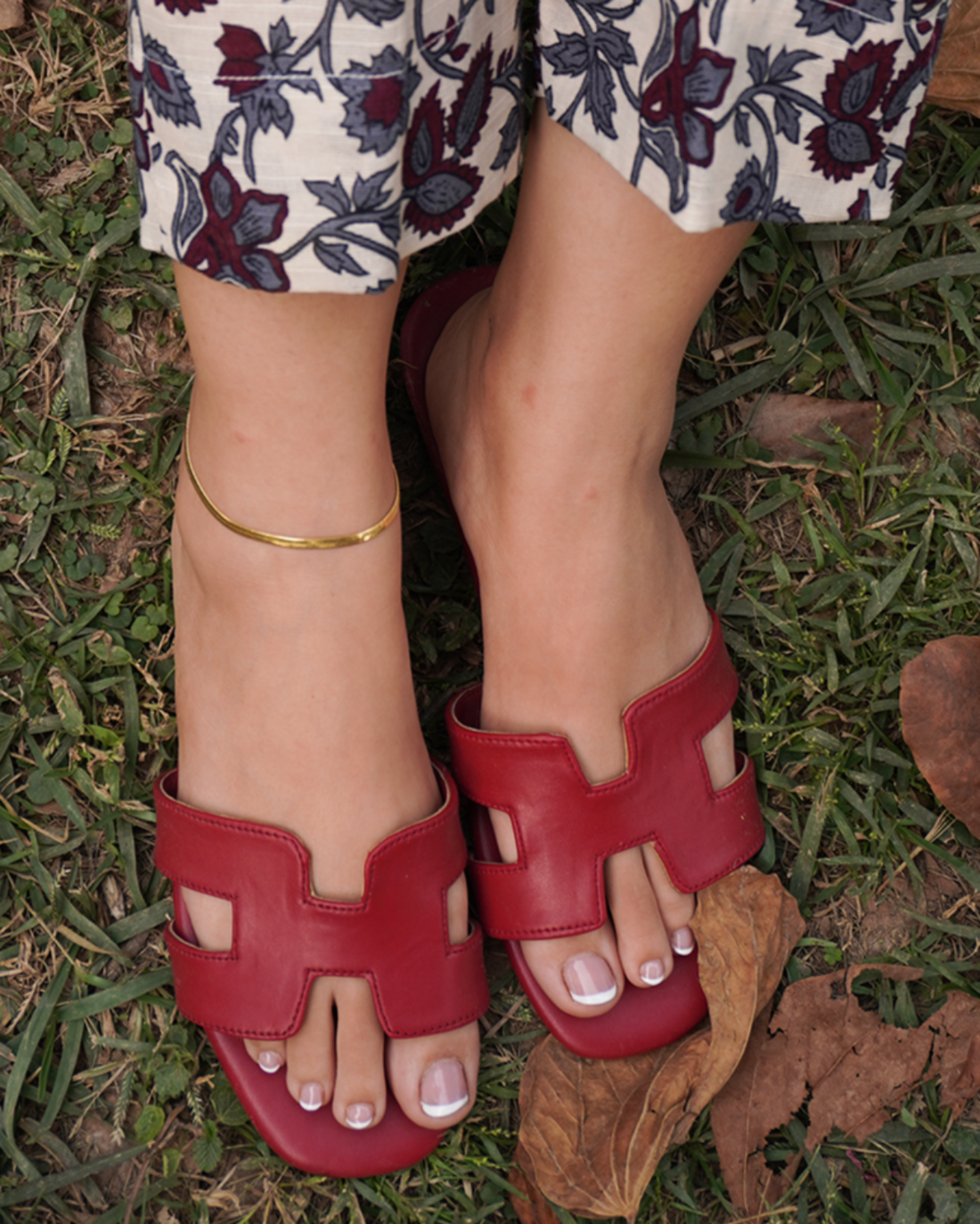 Red H style flats sandals held by a person on a floral fabric background