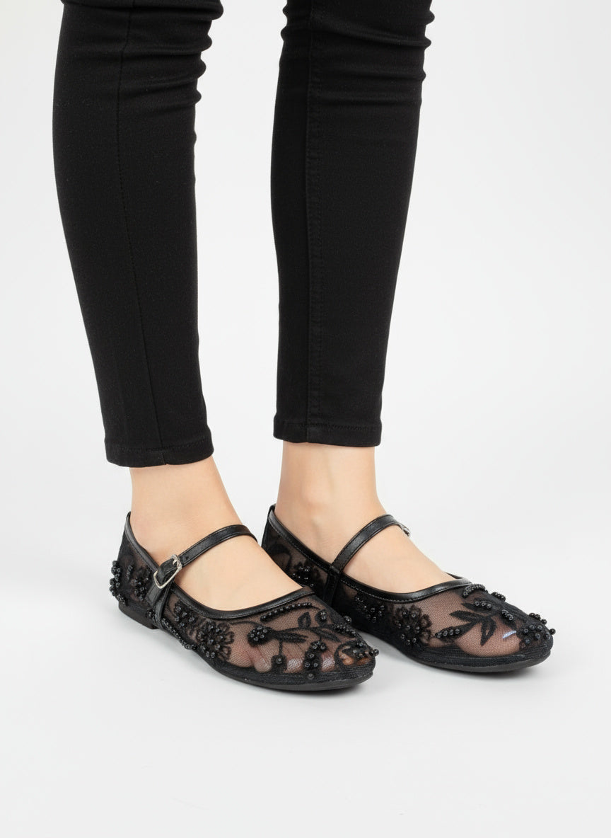 Black floral embroidered flats worn with black pants on a white background