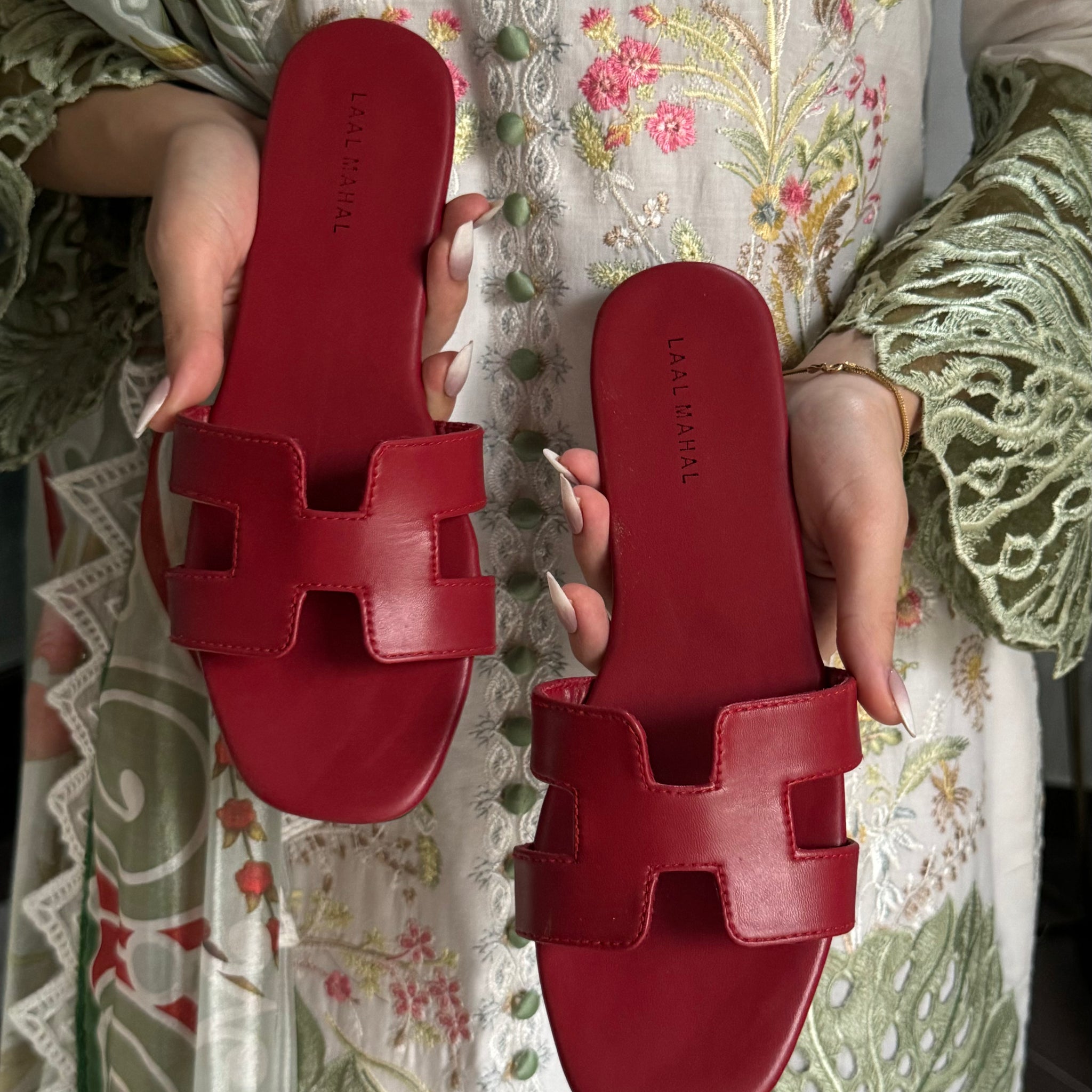 Red H style flats sandals held by a person on a floral fabric background
