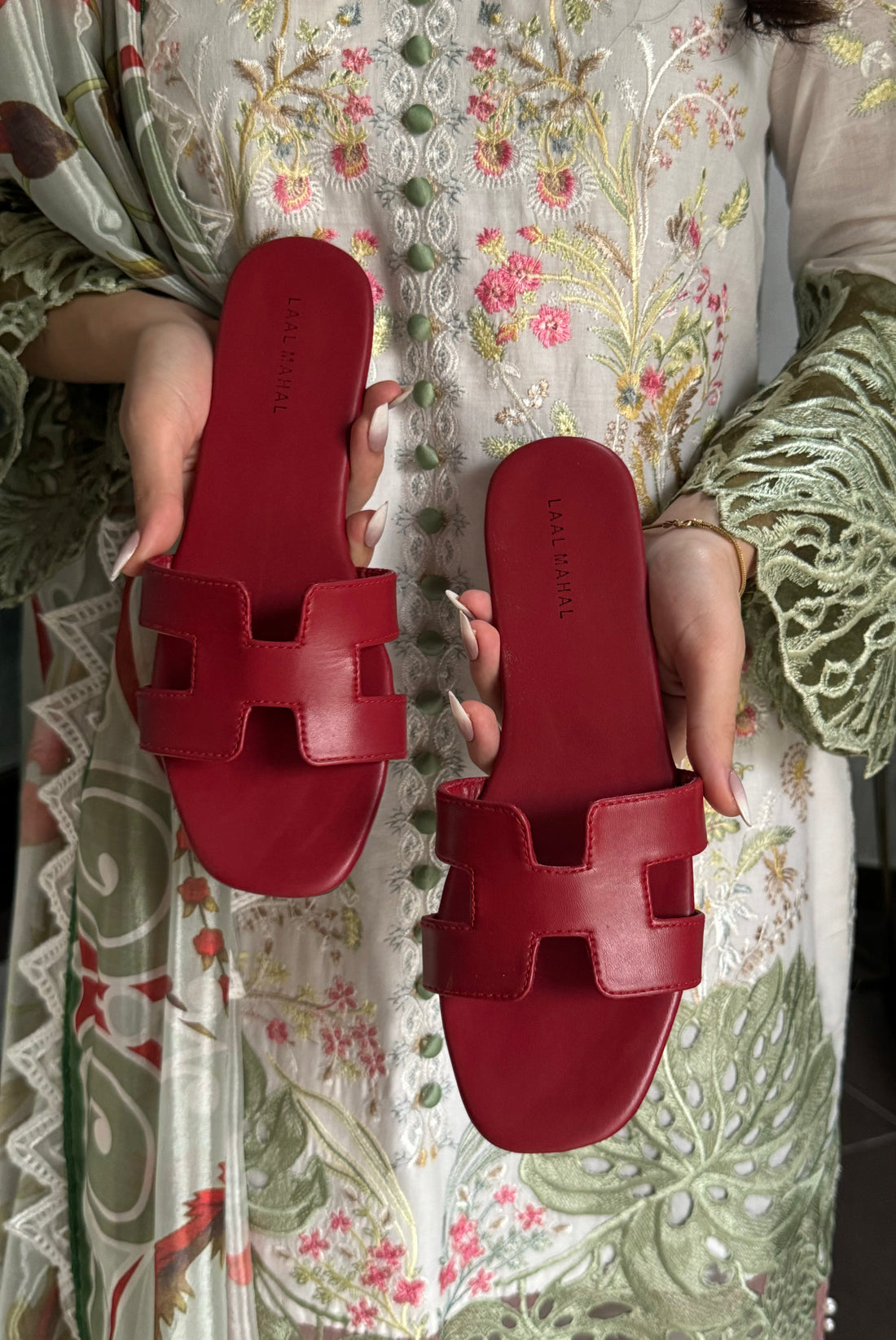 Red H style flats sandals held by a person on a floral fabric background