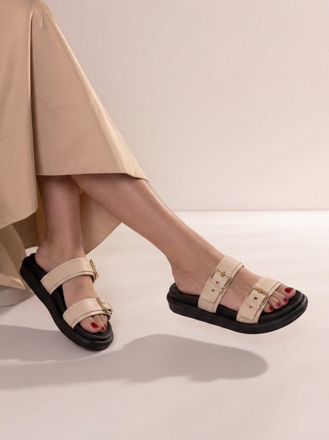 Beige sandals worn with a beige skirt on a light background