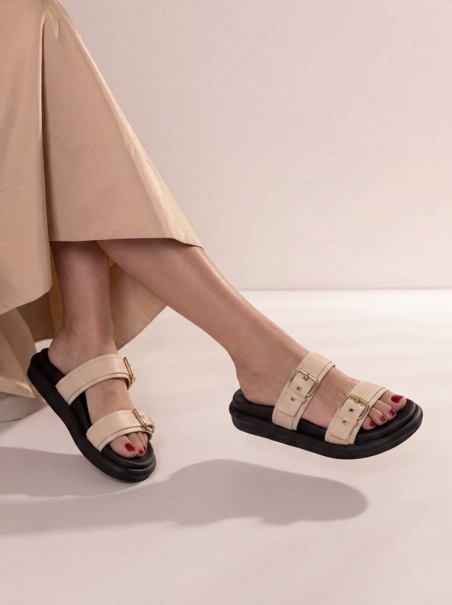 Beige sandals worn with a beige skirt on a light background