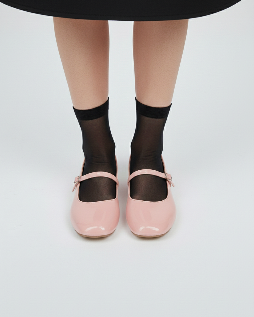 Person wearing black sheer socks with soft pink mary janes flats on a white background